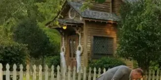 A bride and groom in a wedding pose in front of a rustic wooden chapel and white picket fence at a countryside venue.