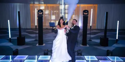 A bride and groom on an LED dance floor with stage lighting, speakers, and a CO2 cold spark effect at a wedding event.