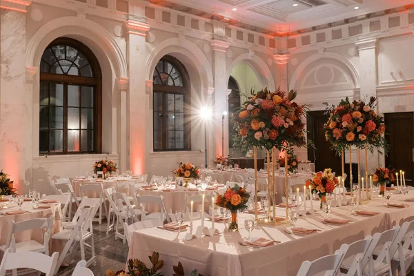 An elegant event hall with white tables, chairs, and floral centerpieces set up for a formal gathering.