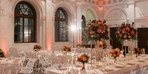 An elegant event hall with white tables, chairs, and floral centerpieces set up for a formal gathering.