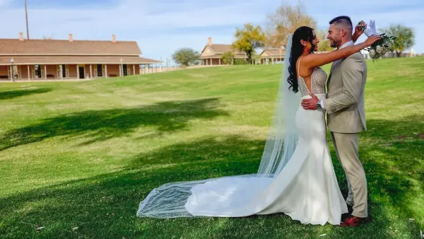 Bride and groom embracing on the grassy grounds of a historic park venue.