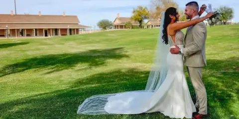 Bride and groom embracing on the grassy grounds of a historic park venue.