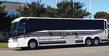 A white and black Discovery Charters motorcoach parked outdoors.