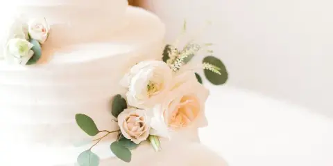 A close-up of a white, multi-tiered wedding cake decorated with white and blush roses and eucalyptus leaves.