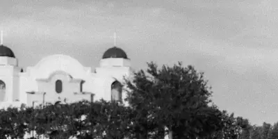 A black and white photo of a bride and groom running hand-in-hand across a lawn with a church in the background.