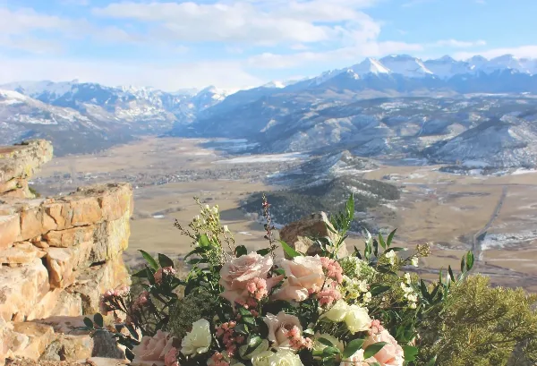 A floral arrangement with pink and white roses and greenery placed on a stone ledge overlooking a mountain valley.