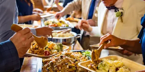 Catering staff serving a buffet of pasta and vegetable dishes to guests at a formal event.