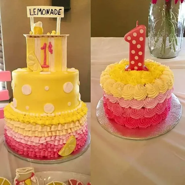 A two-tiered yellow and pink custom cake with ruffled frosting and a lemonade sign, next to a smaller pink and yellow cake with a number 1 candle.