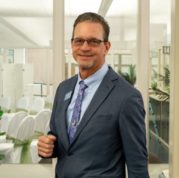 A man in a suit standing in front of a room with chairs decorated for a wedding ceremony.
