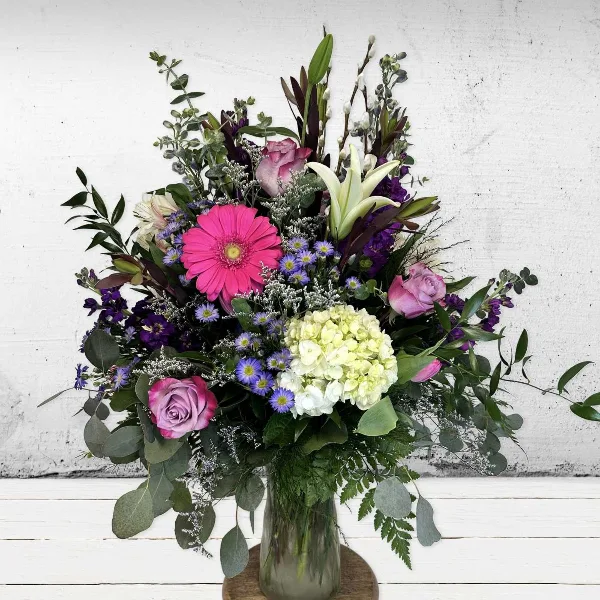 A tall mixed bouquet of pink gerbera, roses, white lilies and green hydrangea in a clear glass vase