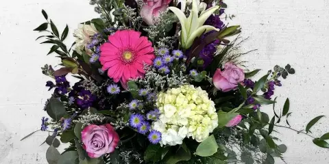 A tall mixed bouquet of pink gerbera, roses, white lilies and green hydrangea in a clear glass vase