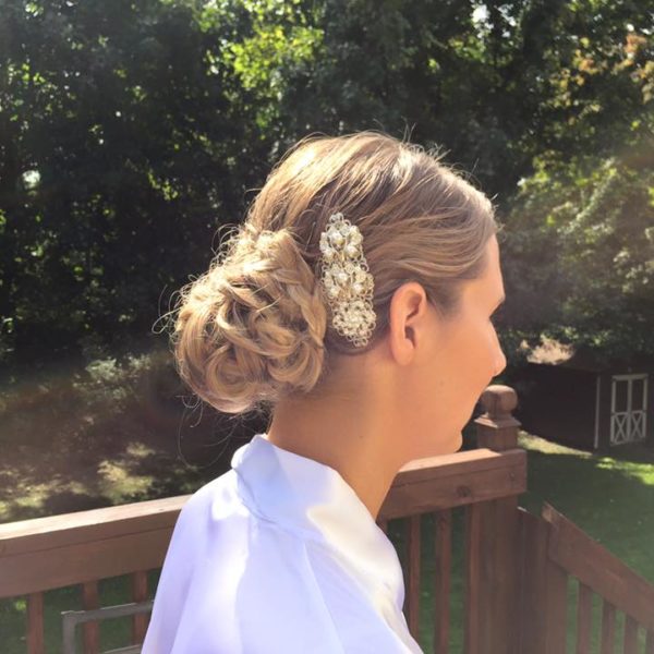 Side profile of a woman with a braided bridal updo and a jeweled hair accessory, standing outdoors.
