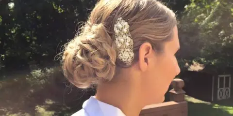 Side profile of a woman with a braided bridal updo and a jeweled hair accessory, standing outdoors.