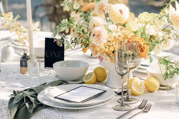 Elegant wedding table setting featuring a floral centerpiece, white plates, wine glasses, and lemons.