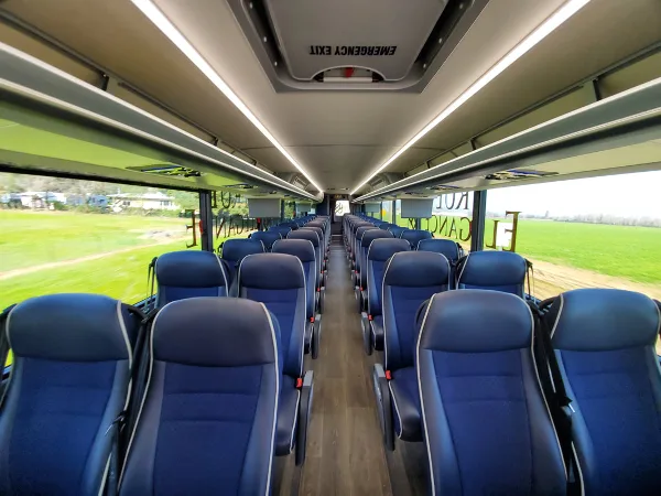 Interior view of a modern charter bus with rows of blue passenger seats and overhead lighting.