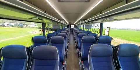 Interior view of a modern charter bus with rows of blue passenger seats and overhead lighting.