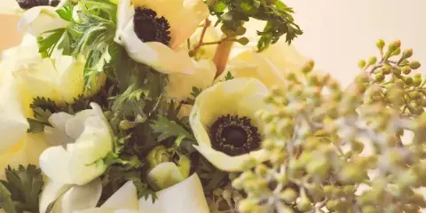 A close-up photograph of a floral arrangement featuring white anemones, cream roses, and green foliage.