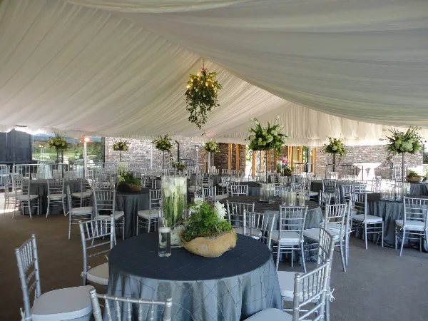 Interior view of a white event tent set up with round tables, grey tablecloths, silver Chiavari chairs, and floral centerpieces.