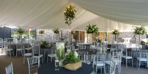 Interior view of a white event tent set up with round tables, grey tablecloths, silver Chiavari chairs, and floral centerpieces.