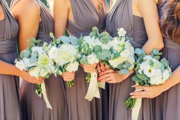Bridesmaids in gray dresses holding white and green wedding bouquets