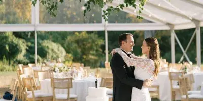 A bride and groom dancing at a wedding reception under a large floral installation in a white tent.