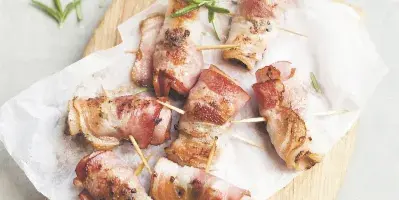 Bacon-wrapped appetizers served on a wooden board with parchment paper and rosemary garnish.