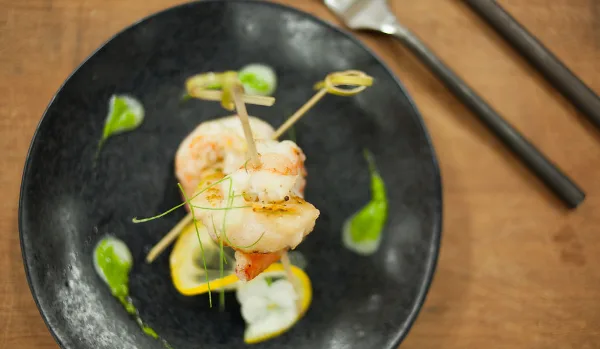 A gourmet shrimp appetizer served on a black plate with lemon slices and green garnish.