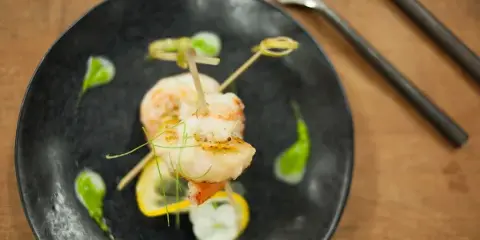 A gourmet shrimp appetizer served on a black plate with lemon slices and green garnish.