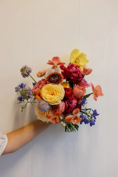 A colorful floral bouquet featuring roses, ranunculus, and other mixed flowers held against a white background.