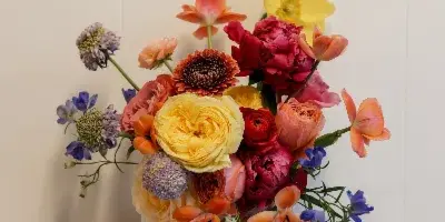 A colorful floral bouquet featuring roses, ranunculus, and other mixed flowers held against a white background.