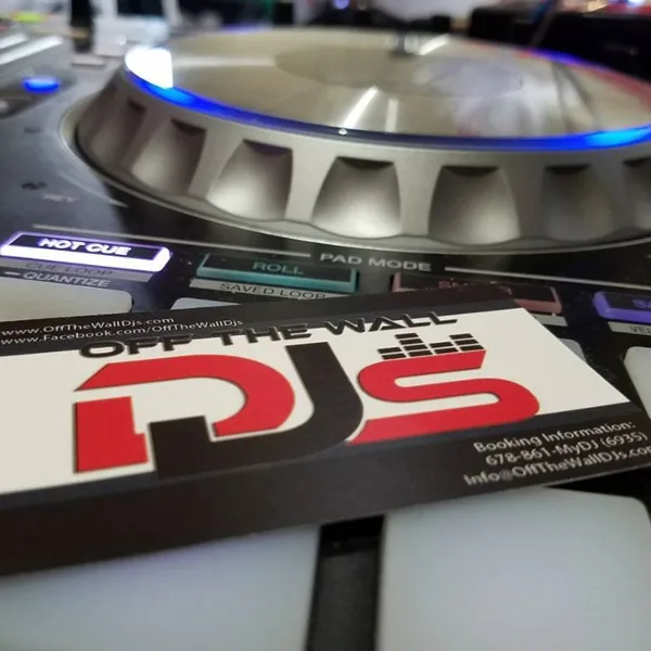 Close-up of a DJ turntable and mixer with an Off The Wall DJs business card placed on the equipment.