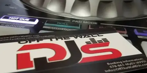 Close-up of a DJ turntable and mixer with an Off The Wall DJs business card placed on the equipment.