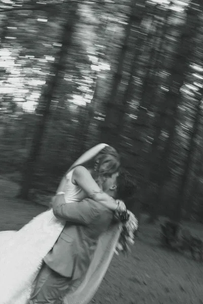 Black and white photograph of a bride and groom sharing a kiss in a wooded area.
