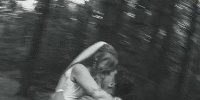 Black and white photograph of a bride and groom sharing a kiss in a wooded area.