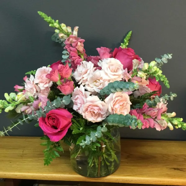A floral arrangement with pink and white roses and greenery in a glass vase