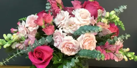 A floral arrangement with pink and white roses and greenery in a glass vase