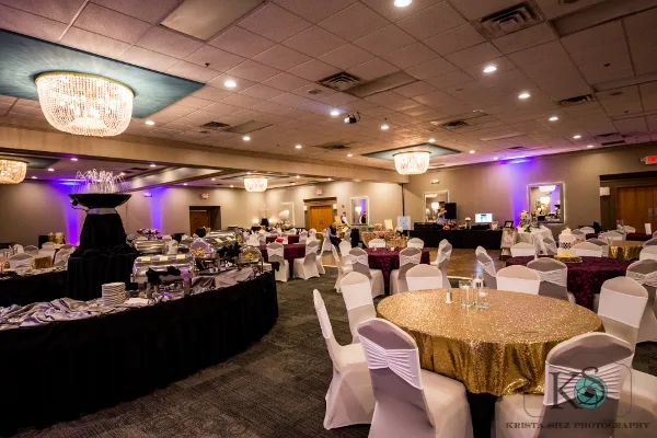 Interior of a wedding banquet hall with round tables, white chair covers, and a catering station.