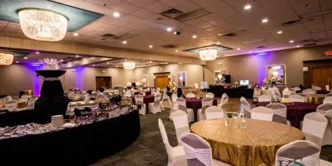 Interior of a wedding banquet hall with round tables, white chair covers, and a catering station.