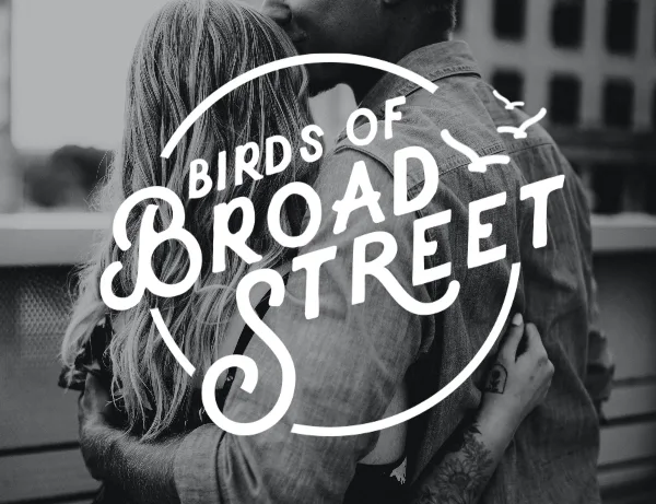 Black and white photograph of a couple embracing with the Birds of Broad Street logo overlaid.