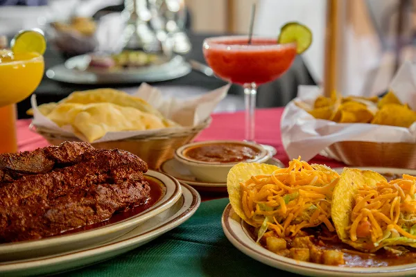 A table setting featuring New Mexican dishes including chili, tacos, and chips alongside margaritas.