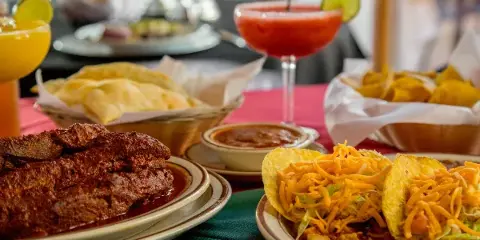 A table setting featuring New Mexican dishes including chili, tacos, and chips alongside margaritas.