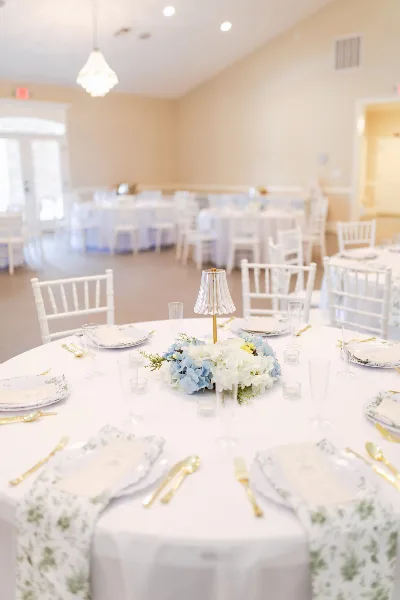 Interior view of a wedding reception hall with white tables, chairs, and floral centerpieces.