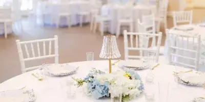 Interior view of a wedding reception hall with white tables, chairs, and floral centerpieces.