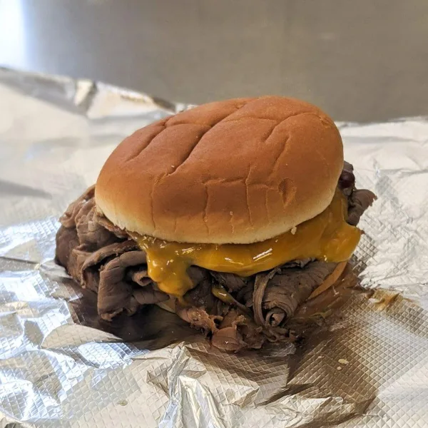 A sandwich with shredded meat and melted cheese on a bun, served on aluminum foil.