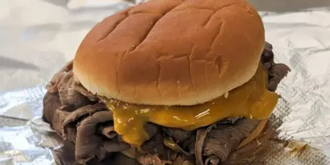 A sandwich with shredded meat and melted cheese on a bun, served on aluminum foil.