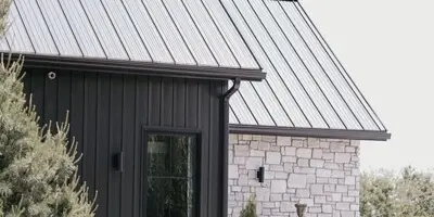 Exterior view of a modern wedding venue building with a dark metal roof, stone wall, and a tiered fountain in the foreground.