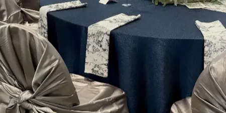 Reception tables set with navy tablecloths, patterned runners, and champagne-colored chair covers with self-tie sashes.