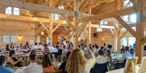 Interior view of a timber frame barn venue with guests seated at tables and a band performing on stage.