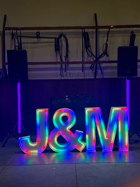A stage setup featuring a large, colorful LED neon sign reading 'J&M' flanked by professional speakers and lighting equipment.