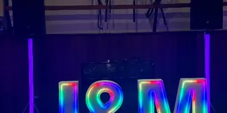 A stage setup featuring a large, colorful LED neon sign reading 'J&M' flanked by professional speakers and lighting equipment.